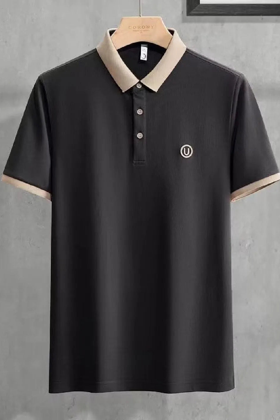 Black polo shirt with beige collar on a hanger against a gray background