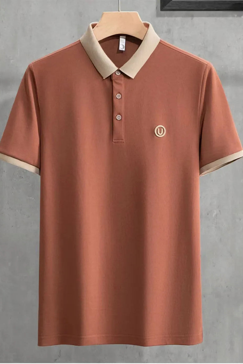Brown polo shirt with beige collar on a hanger against a gray background