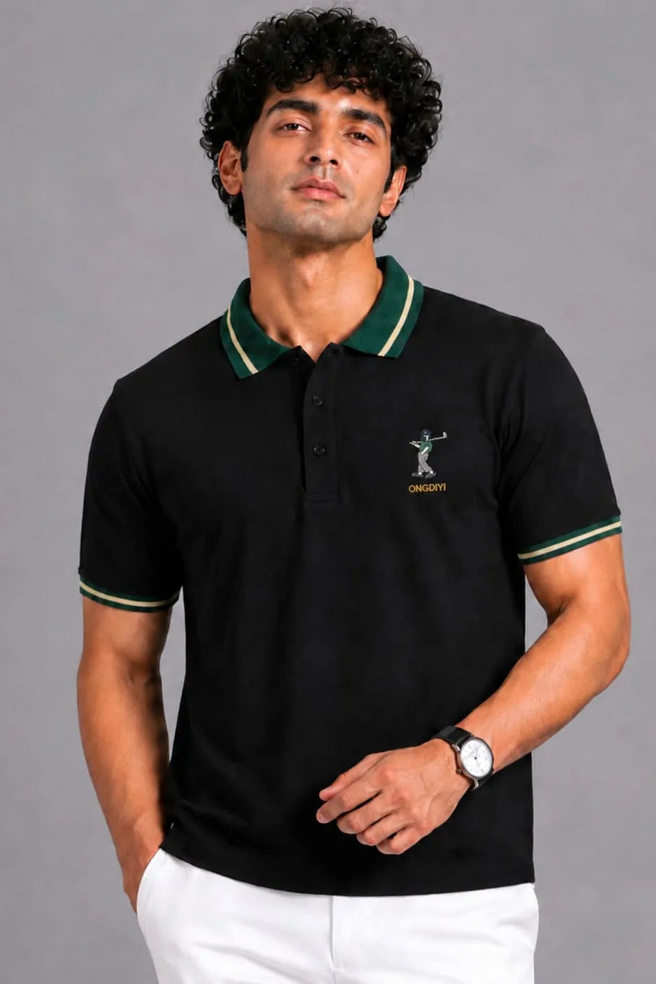 A man wearing a black short-sleeve polo shirt with green and white striped collar and sleeve cuffs, featuring a small embroidered golfer logo and the brand name 'DASHPA' on the left chest, paired with white trousers against a solid gray studio background.