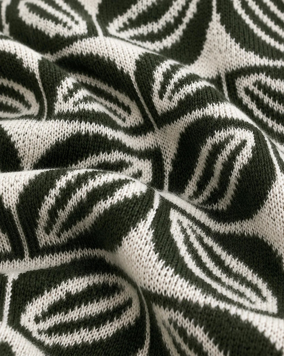 Close-up of the deep green and white repeating leaf-motif jacquard polo knit texture