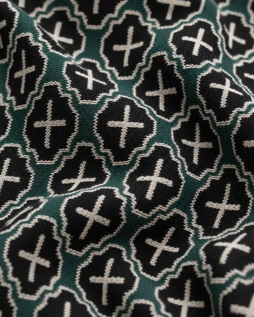 Close-up of the deep teal green and white mosaic geometric jacquard polo knit texture